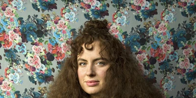 Woman with curly brown hair against a background print of roses. This art paper has a smooth surface and has been the number one choice for artists since its inception.